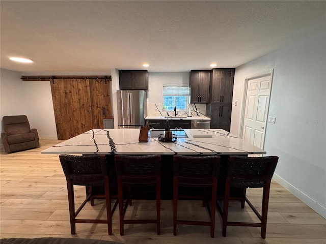 dining room with light wood finished floors, a barn door, baseboards, and recessed lighting