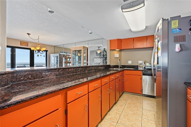 kitchen with light tile patterned floors, appliances with stainless steel finishes, an inviting chandelier, a textured ceiling, and dark stone counters