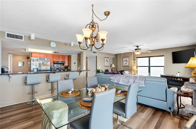 dining space with sink, ceiling fan with notable chandelier, a textured ceiling, and light wood-type flooring