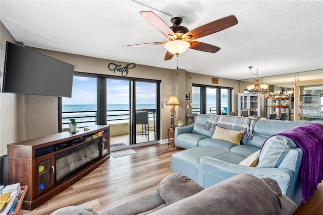 living room featuring ceiling fan with notable chandelier, a textured ceiling, and light wood-type flooring