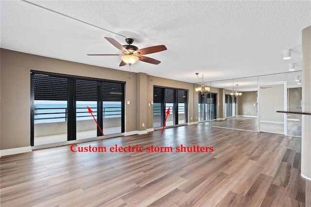 unfurnished living room featuring ceiling fan with notable chandelier, light hardwood / wood-style floors, and a textured ceiling