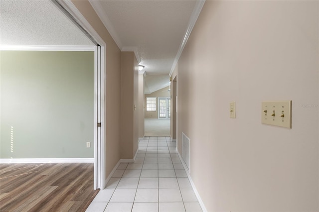 corridor featuring ornamental molding, vaulted ceiling, a textured ceiling, and light tile patterned floors