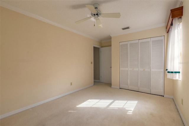 unfurnished bedroom with crown molding, light colored carpet, ceiling fan, and a closet