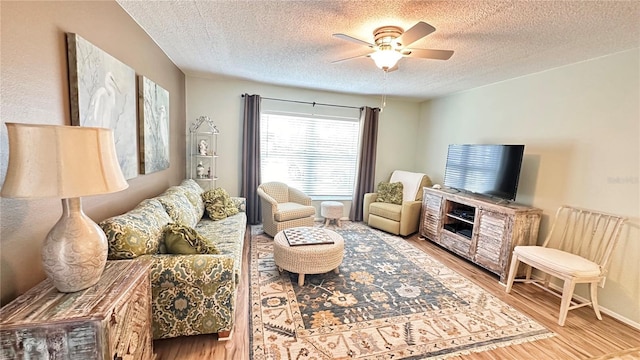 living room with ceiling fan, a textured ceiling, and light wood-type flooring