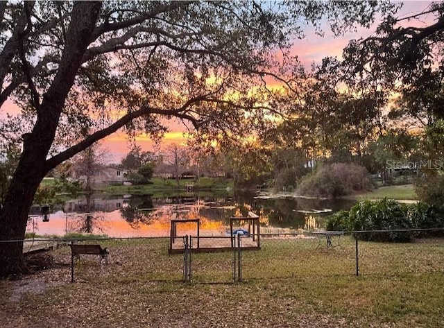 view of community featuring a water view, a gate, fence, and a lawn