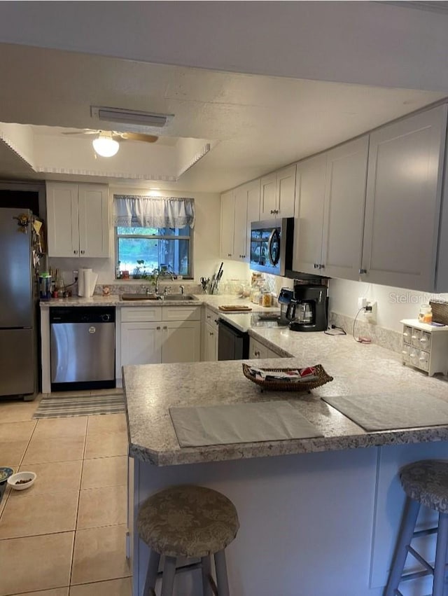 kitchen with a breakfast bar, a peninsula, light tile patterned flooring, stainless steel appliances, and a sink