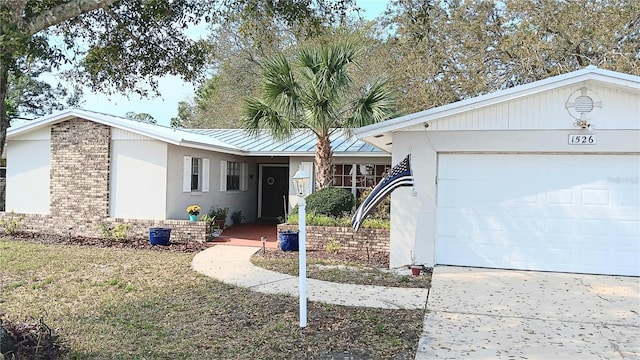 ranch-style house featuring stucco siding, a garage, brick siding, and metal roof