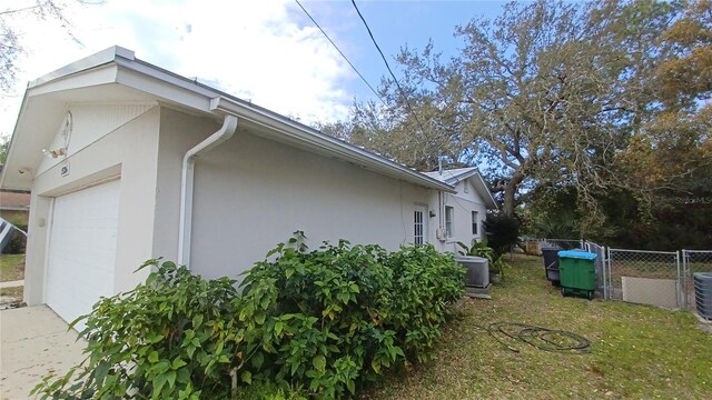 view of side of home with stucco siding, cooling unit, a garage, and fence