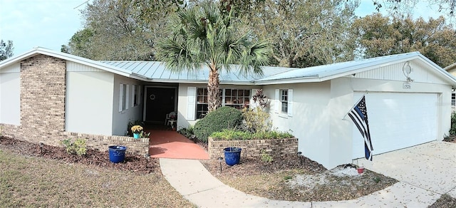 ranch-style house with stucco siding, a standing seam roof, an attached garage, metal roof, and brick siding