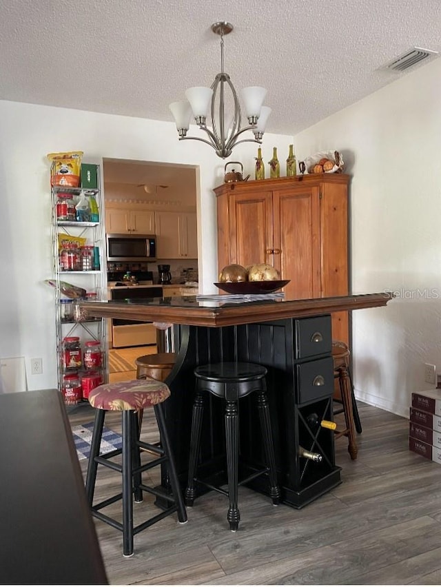 bar with stainless steel microwave, light wood-type flooring, electric range, a notable chandelier, and a textured ceiling