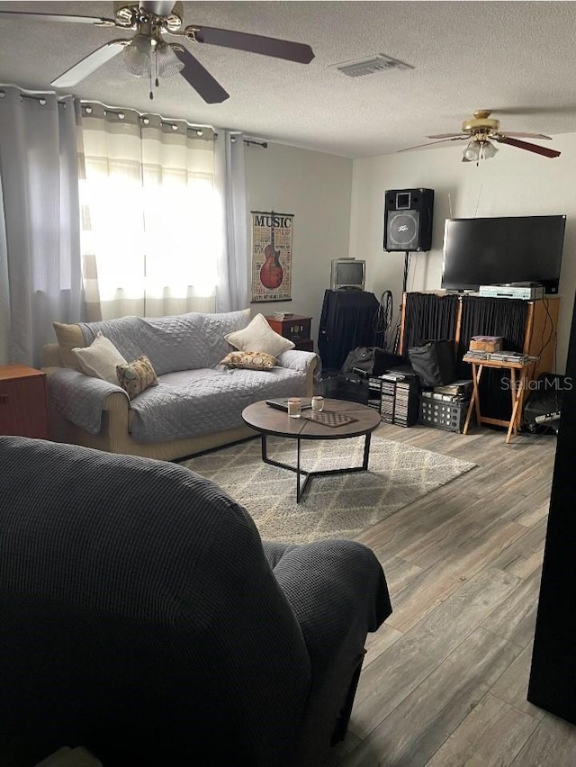 living room with a ceiling fan, wood finished floors, visible vents, and a textured ceiling