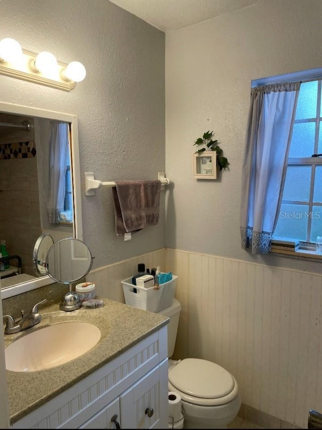 bathroom featuring vanity, toilet, a textured wall, and wainscoting