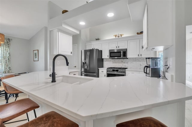 kitchen with white cabinets, light stone counters, a peninsula, stainless steel appliances, and a sink