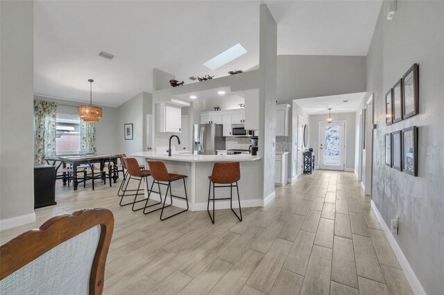 kitchen with light hardwood / wood-style flooring, hanging light fixtures, stainless steel appliances, white cabinets, and a kitchen bar