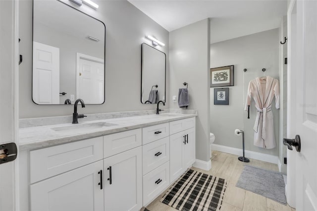 full bathroom featuring double vanity, baseboards, toilet, and a sink