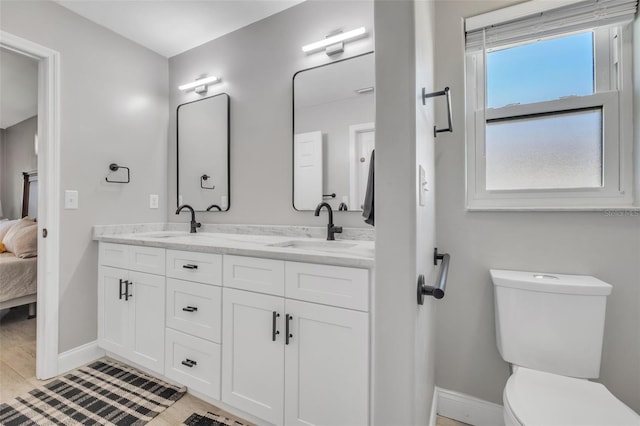 full bath featuring double vanity, baseboards, connected bathroom, toilet, and a sink