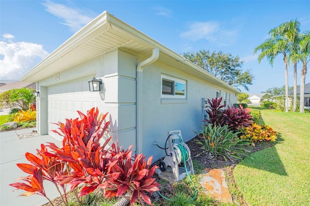 view of side of home with a yard, driveway, an attached garage, and stucco siding