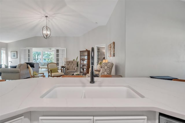 kitchen featuring lofted ceiling, a sink, open floor plan, light stone countertops, and pendant lighting