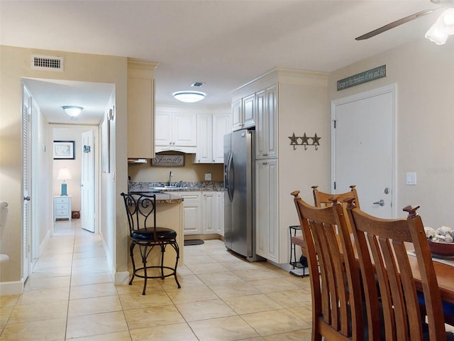 kitchen featuring stone counters, white cabinetry, stainless steel fridge, a kitchen breakfast bar, and ceiling fan