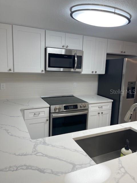 kitchen featuring light stone counters, appliances with stainless steel finishes, tasteful backsplash, and white cabinets