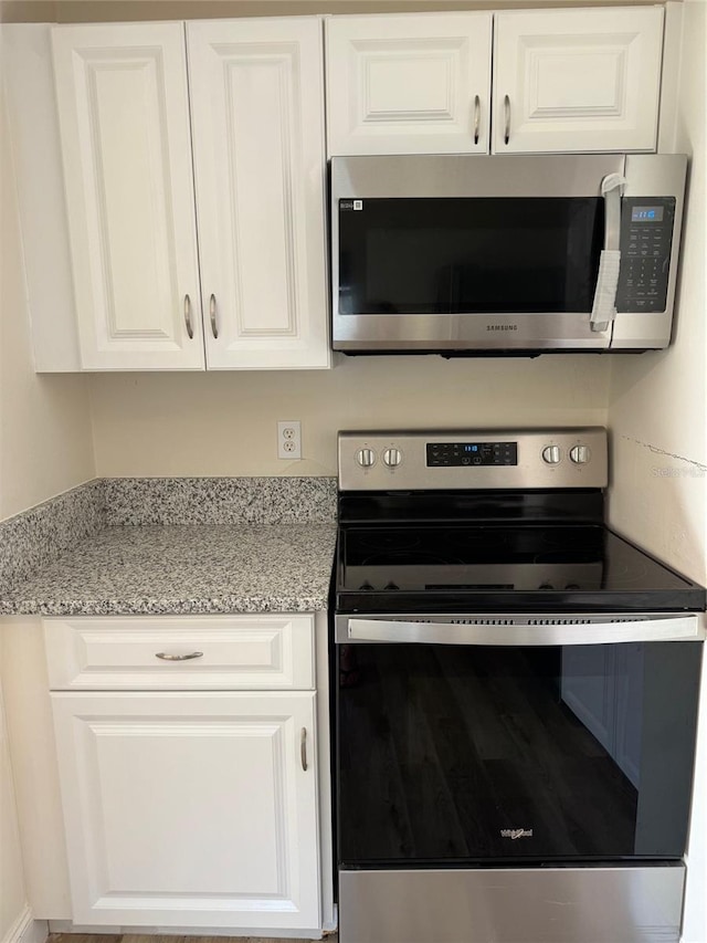 kitchen featuring stainless steel appliances, white cabinetry, and light stone countertops