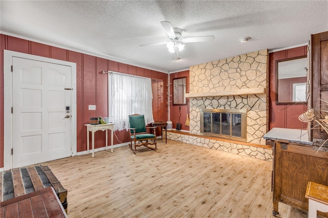 interior space with a stone fireplace, light hardwood / wood-style flooring, a textured ceiling, and ceiling fan