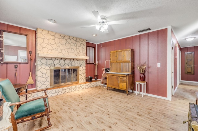 sitting room featuring ceiling fan, a stone fireplace, a textured ceiling, and light wood-type flooring