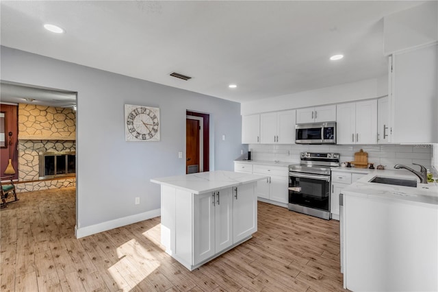 kitchen with sink, appliances with stainless steel finishes, a kitchen island, a fireplace, and white cabinets