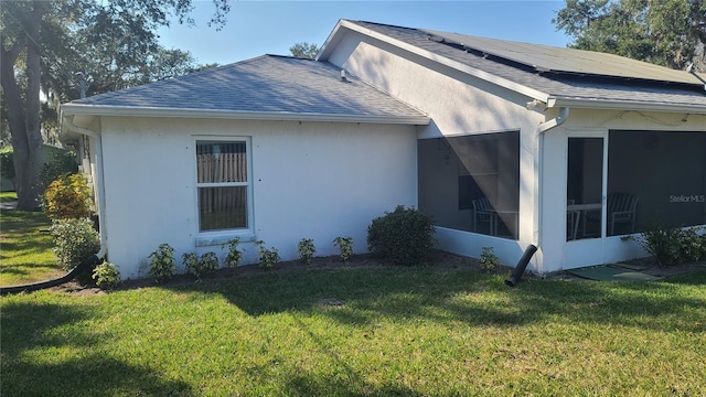 view of side of property featuring a sunroom, a lawn, and solar panels