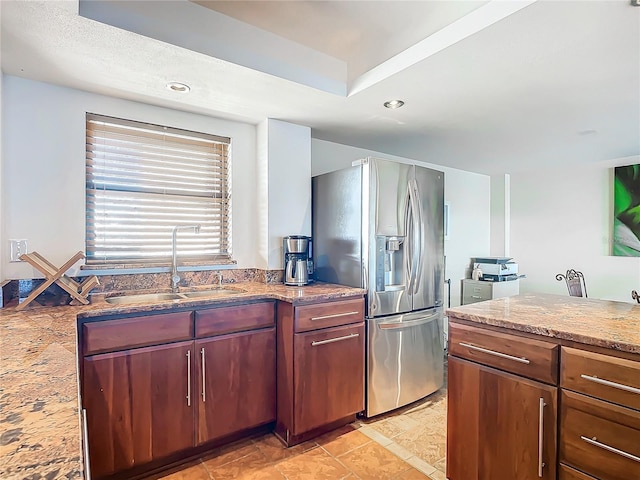 kitchen with stainless steel refrigerator with ice dispenser, light stone countertops, and sink