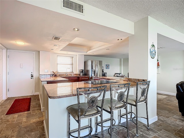 kitchen with kitchen peninsula, stainless steel fridge, a kitchen breakfast bar, a tray ceiling, and a textured ceiling