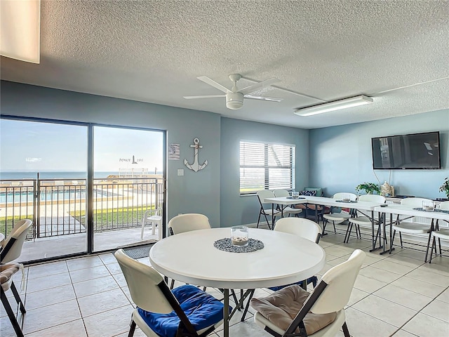 tiled dining area with a textured ceiling, ceiling fan, and a water view