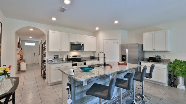 kitchen featuring sink, white cabinetry, a center island with sink, appliances with stainless steel finishes, and light stone countertops