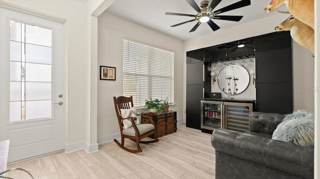 living area featuring wine cooler, ceiling fan, bar area, and light wood-type flooring