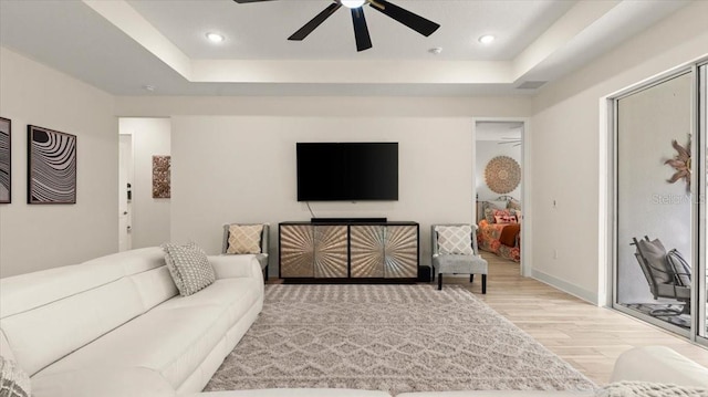 living room featuring a raised ceiling, ceiling fan, and light hardwood / wood-style flooring