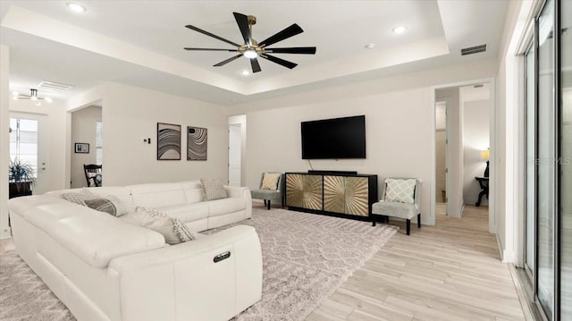 living room featuring light hardwood / wood-style flooring, a raised ceiling, and ceiling fan