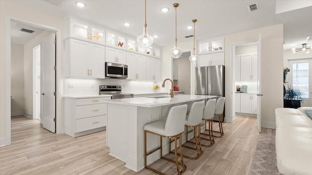 kitchen featuring appliances with stainless steel finishes, sink, white cabinets, backsplash, and a kitchen island with sink