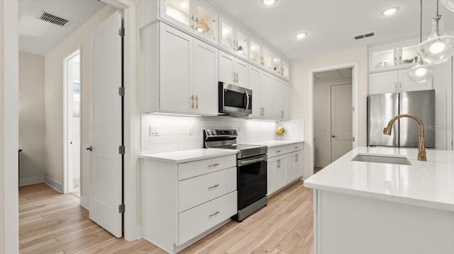 kitchen with appliances with stainless steel finishes, sink, pendant lighting, and white cabinets