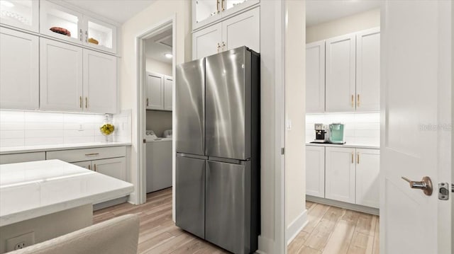 kitchen featuring white cabinets, washing machine and dryer, stainless steel fridge, and light hardwood / wood-style flooring