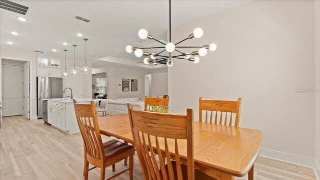 dining area with sink, a notable chandelier, and light wood-type flooring