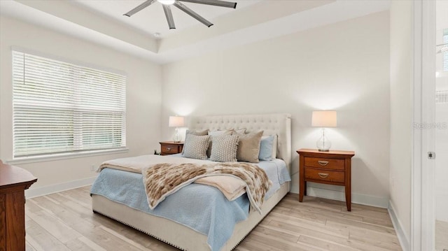 bedroom with a tray ceiling, light hardwood / wood-style flooring, and ceiling fan