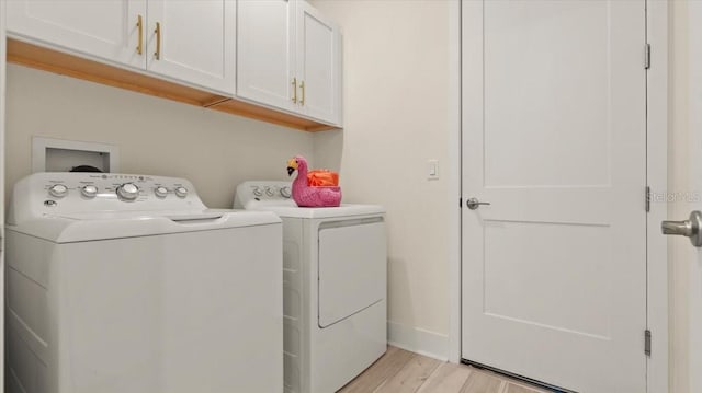 clothes washing area featuring cabinets, washing machine and clothes dryer, and light wood-type flooring