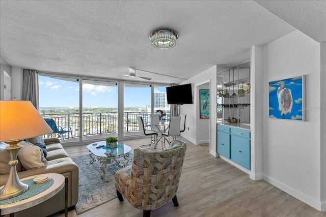 living room featuring expansive windows, ceiling fan, light hardwood / wood-style flooring, and a textured ceiling