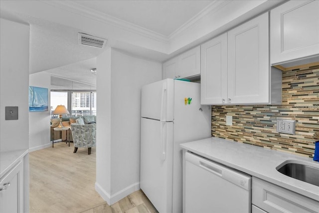 kitchen with crown molding, white appliances, light hardwood / wood-style flooring, backsplash, and white cabinets