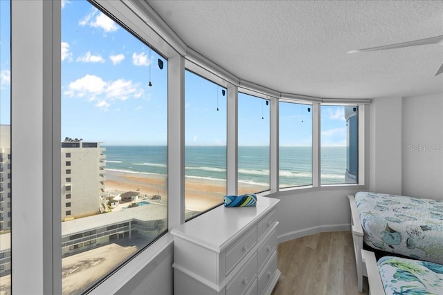 bedroom with a view of the beach, light wood-type flooring, a textured ceiling, and a water view