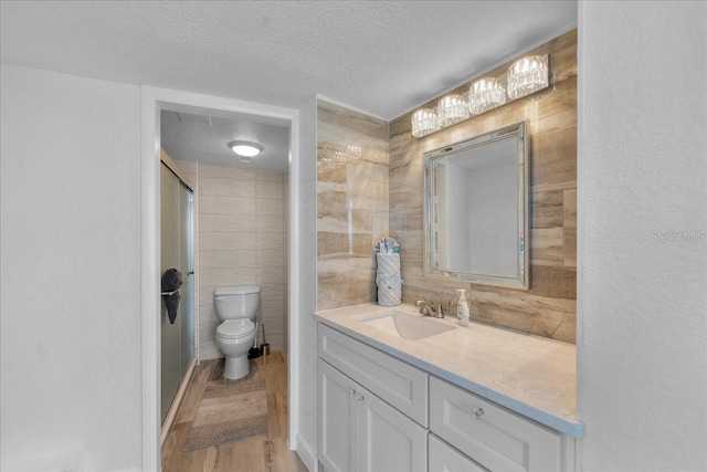 bathroom with a shower with shower door, wood-type flooring, tile walls, vanity, and a textured ceiling