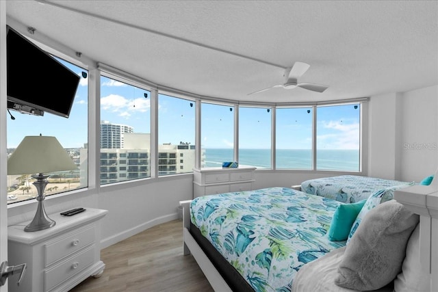 bedroom featuring multiple windows, light wood-type flooring, a textured ceiling, and a water view