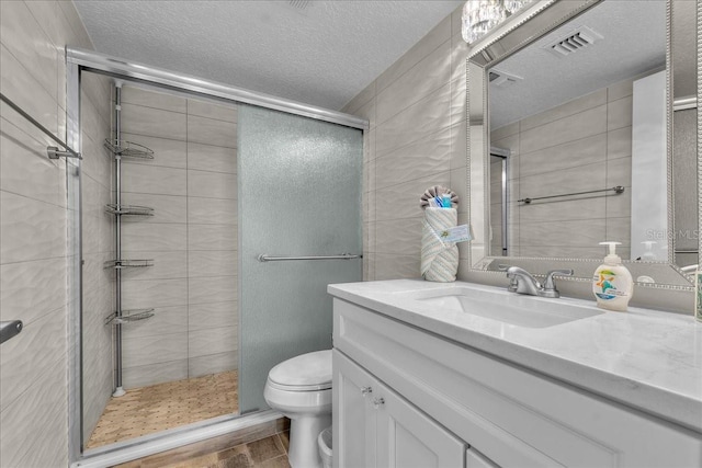 bathroom with wood-type flooring, vanity, toilet, a shower with door, and a textured ceiling