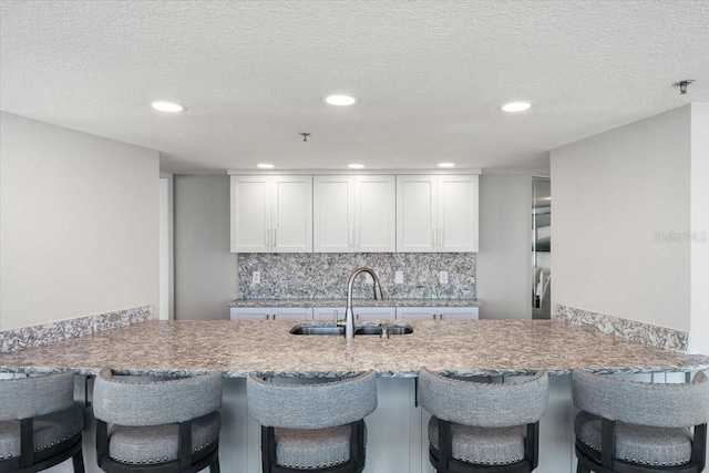 kitchen featuring a breakfast bar, tasteful backsplash, sink, white cabinets, and a textured ceiling