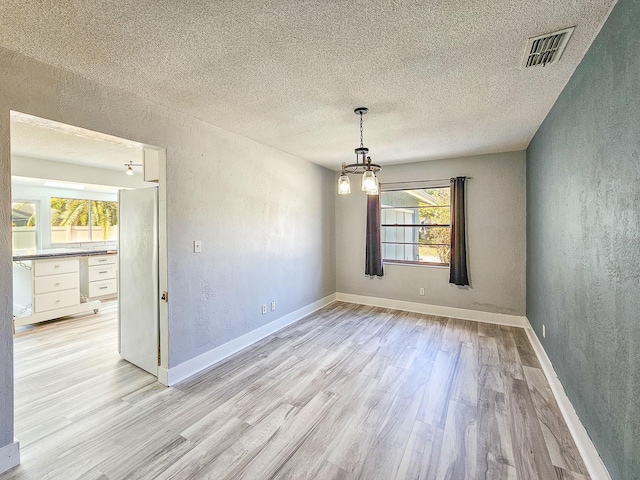 spare room with a chandelier, a textured ceiling, and light wood-type flooring